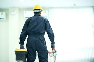 a ásia jovem técnico serviço homem vestindo azul uniforme verificando, profissional ar condicionador instalador mantendo moderno interior ar condicionador espaço para texto foto