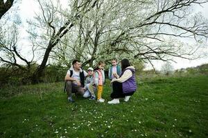 família com três crianças dentro Primavera Prado em a fundo do uma floração árvore. foto