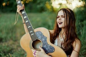 lindo mulher jogando guitarra dentro natureza dentro uma hippie verão olhar, cantando canções estilo do vida sem preocupações foto