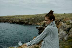 mulher dentro uma cinzento suéter carrinhos em uma rochoso costa natureza estilo de vida foto