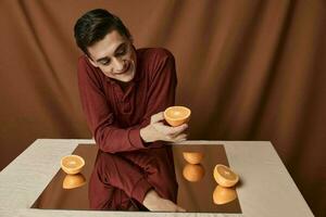 uma homem dentro uma camisa às uma mesa com uma espelho reflexão laranjas tecido fundo foto