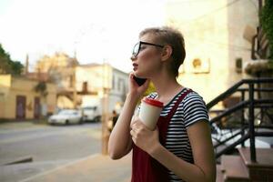 mulher com curto cabelo copo do café com óculos falando em a telefone foto