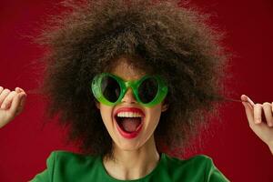 alegre mulher dentro verde óculos afro Penteado vermelho fundo foto