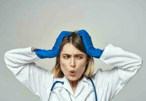 emocional mulher dentro azul médico luvas toques dela cabeça com dela mãos em uma luz fundo foto