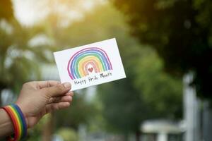 'feliz orgulho mês' cartão segurando dentro mão que tem arco Iris pulseira por aí isto, conceito para cumprimento todos pessoas para estar feliz dentro a lgbtq eventos por aí a mundo dentro orgulho mês. foto