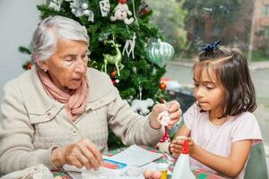 pequeno menina tendo Diversão enquanto fazer Natal natividade trabalhos manuais com dela avó - real família foto