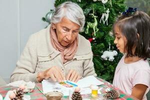 pequeno menina tendo Diversão enquanto fazer Natal natividade trabalhos manuais com dela avó - real família foto
