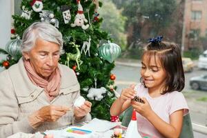 pequeno menina tendo Diversão enquanto fazer Natal natividade trabalhos manuais com dela avó - real família foto