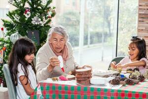 pequeno meninas tendo Diversão enquanto fazer Natal natividade trabalhos manuais com seus avó - real família foto