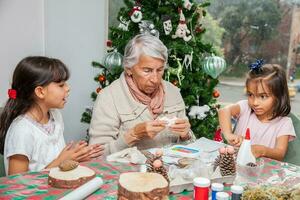 pequeno meninas tendo Diversão enquanto fazer Natal natividade trabalhos manuais com seus avó - real família foto