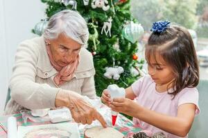 pequeno menina tendo Diversão enquanto fazer Natal natividade trabalhos manuais com dela avó - real família foto