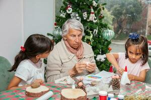 pequeno meninas tendo Diversão enquanto fazer Natal natividade trabalhos manuais com seus avó - real família foto