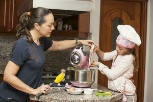 mãe e filha tendo Diversão dentro a cozinha cozimento junto. preparando bolos de copo com mãe foto