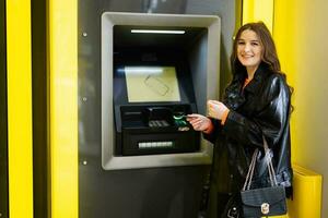 jovem morena menina retirada dinheiro a partir de crédito cartão às amarelo atm. foto