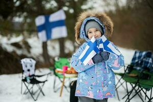 finlandês pequeno menina com Finlândia bandeiras em uma agradável inverno dia. nórdico escandinavo pessoas. foto