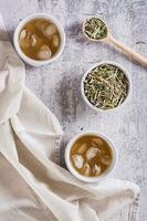 gelado verde japonês hojicha chá dentro copos e folhas dentro uma tigela em a mesa topo e vertical Visão foto