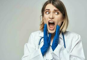 mulher médico com aberto boca dentro uma médico vestido azul luvas estetoscópio foto