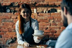 bonita mulher garçom traz café serviço tijolo parede foto