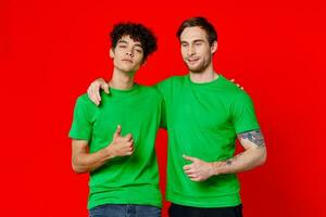 dois homens abraçando dentro verde Camisetas em uma vermelho fundo foto