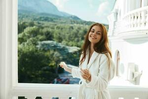 alegre mulher dentro uma branco roupão segurando dela cabelo posando em a sacada foto