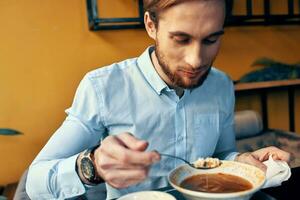 uma homem come borscht com azedo creme dentro uma restaurante às uma mesa dentro uma cafeteria e uma Assistir em dele mão foto