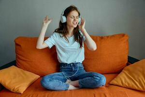 retrato do uma mulher sentado em a sofá às casa ouvindo para música em fones de ouvido estilo de vida foto