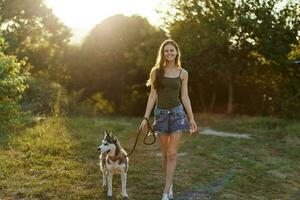 mulher e dela rouco cachorro caminhando alegremente em a Relva dentro a parque sorrir com dentes dentro a outono andar com dela bicho de estimação, viagem com uma cachorro amigo foto