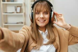 fofa jovem Loiras aluna senhora trabalhador autonomo dentro caloroso suéter dentro fones de ouvido ouço fav canções sentado dentro poltrona às moderno casa interior. música Tempo relaxante legal lista de reprodução conceito. Largo selfie Visão foto