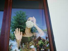 mascarado mulher inclinado contra janela quarentena banimento foto