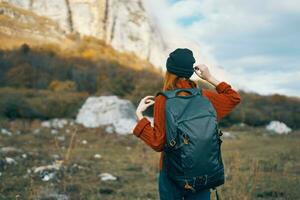 uma viajante dentro uma suéter e uma chapéu é em repouso dentro a montanhas dentro natureza e uma mochila em dela costas foto