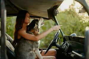 uma lindo jovem mulher senta atrás a roda do dela carro juntos com uma rouco procriar cachorro e sorrisos alegremente goza a viagem foto