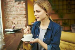 bonita mulher sentado às uma cafeteria mesa com uma copo do café café da manhã estilo de vida foto