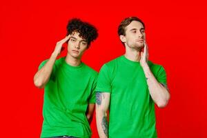 dois amigos dentro verde Camisetas estão em pé Próximo para lata com seus mãos emoções vermelho fundo foto