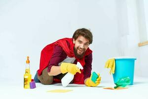 uma homem com limpeza suprimentos dentro uma vermelho capa de chuva em a chão do uma casa interior profissional foto