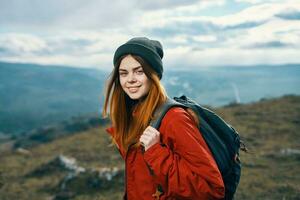 retrato do uma viajante dentro uma vermelho Jaqueta e chapéu e com uma mochila ao ar livre dentro a montanhas fresco ar foto