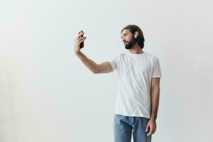 uma masculino blogueiro filmar ele mesmo em dele telefone e conversando com pessoas conectados com uma sorrir dentro uma branco camiseta contra uma branco parede foto