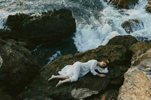 lindo jovem mulher deitado em dela costas em uma rochoso Beira Mar Visão a partir de acima foto