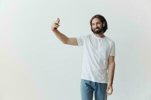 uma masculino blogueiro filmar ele mesmo em dele telefone e conversando com pessoas conectados com uma sorrir dentro uma branco camiseta contra uma branco parede foto