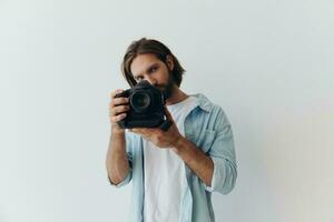 homem hipster fotógrafo dentro uma estúdio contra uma branco fundo segurando uma profissional Câmera e configuração isto acima antes tiroteio. estilo de vida trabalhos Como uma freelance fotógrafo foto