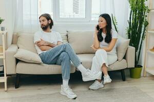 uma jovem casado casal sentado em a sofá não falando para cada outro, família querelas e descontentamento. estilo de vida dentro mal entendido e falta de vontade para trabalhos em a relação para amor foto