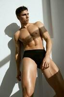 atraente desportivo homem com uma bombeado muscular corpo dentro Sombrio calção luz fundo foto
