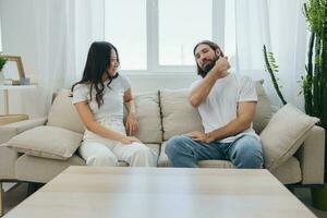 uma homem e uma mulher sentado às casa em a sofá dentro branco à moda Camisetas e conversando alegremente sorridente e rindo às lar. masculino e fêmea amizade foto