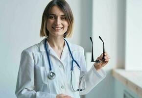 profissional médico mulher segurando óculos dentro dela mão e estetoscópio por aí dela pescoço foto