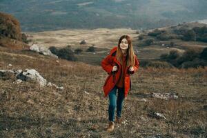 viagem turismo jovem mulher dentro vermelho Jaqueta e jeans com mochila dentro a montanhas dentro outono foto