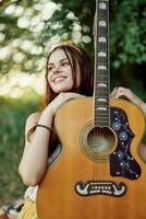 jovem hippie mulher com eco imagem sorridente e olhando para dentro a Câmera com guitarra dentro mão dentro natureza em uma viagem foto