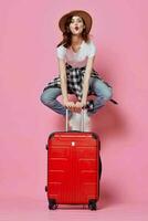 alegre mulher turista senta em uma vermelho mala de viagem voar aeroporto foto
