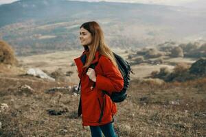 ruivo mulher dentro Jaqueta com mochila viagem caminhada montanhas fresco ar foto