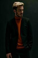 à moda homem com uma elegante Penteado e dentro uma couro Jaqueta laranja suéter Preto fundo foto