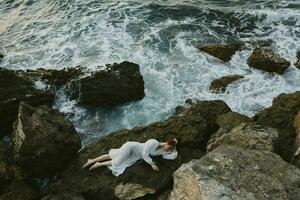 descalço mulher dentro uma branco vestir deitado em uma pedra dentro uma branco vestir período de férias conceito foto