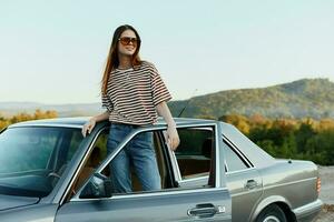 uma jovem mulher motorista parece Fora do a carro às a outono panorama e sorrisos satisfatoriamente foto